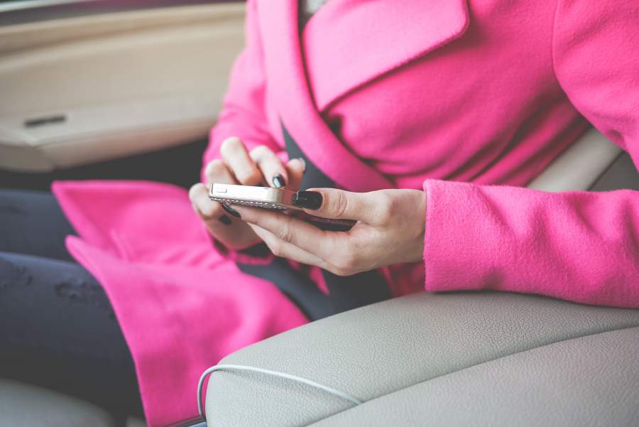 Frau in rosa Mantel nutz ihr Smartphone in einem Auto