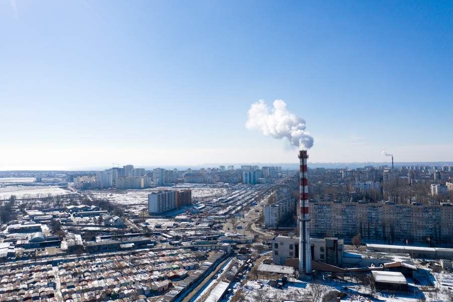 Kleine Rauchwolke an einem hohen Kamin über einem Industriegelände mit Parkplatz in der Nähe vor einem klaren blauen Himmel