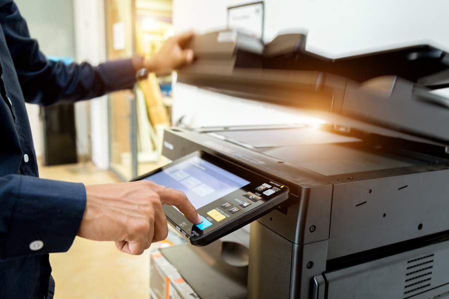 Mann steht am Laser-Drucker, um etwas zu kopieren und drückt den Start-Knopf.