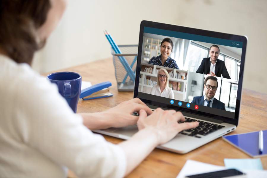 Geschäftsleute in einer Webkonferenz, Blick über die Schulter einer Teilnehmerin in Online-Meeting mit geteiltem Bildschirm mit vier weiteren Personen