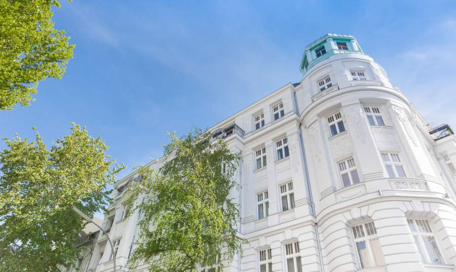 Drei Bäume vor der weißen Fassade eines Altbau-Apartments in der Stadt.