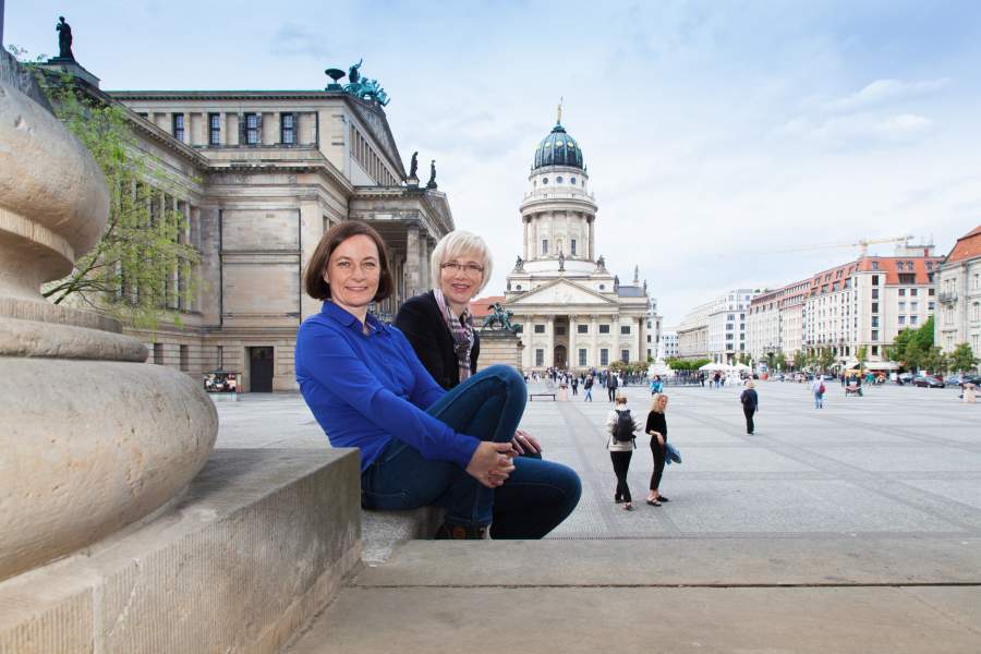 Die zwei Imagefilm-Expertinnen Susanne Rodeck und Katarzyna Koslinska von avidere Erklärvideo- und Imagefilm-Agentur Berlin sitzen gemeinsam auf einer Treppen in der Stadt.