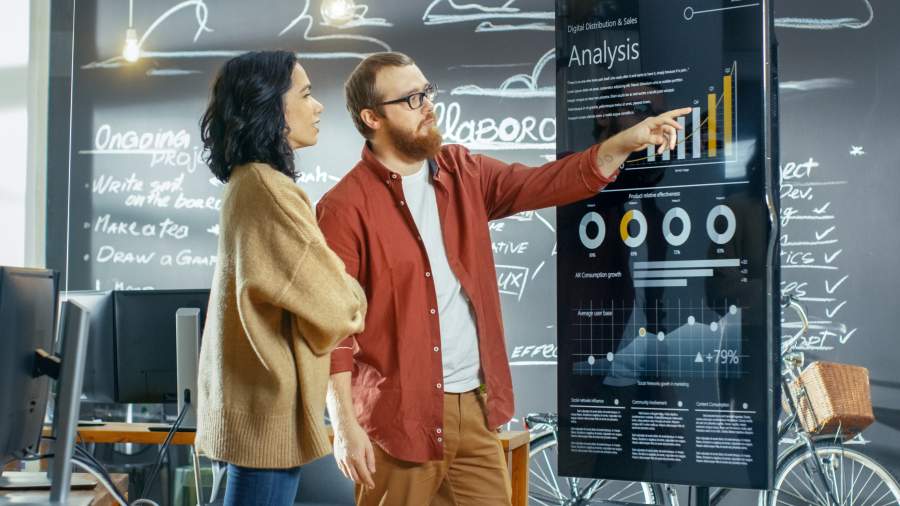 Frau und Mann stehen vor einer Chart und interpretieren Diagramme, Schriftzu "Analysis"