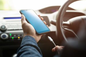 Mann steckt sein Handy während des Fahrens an ein Autoladegerät an.