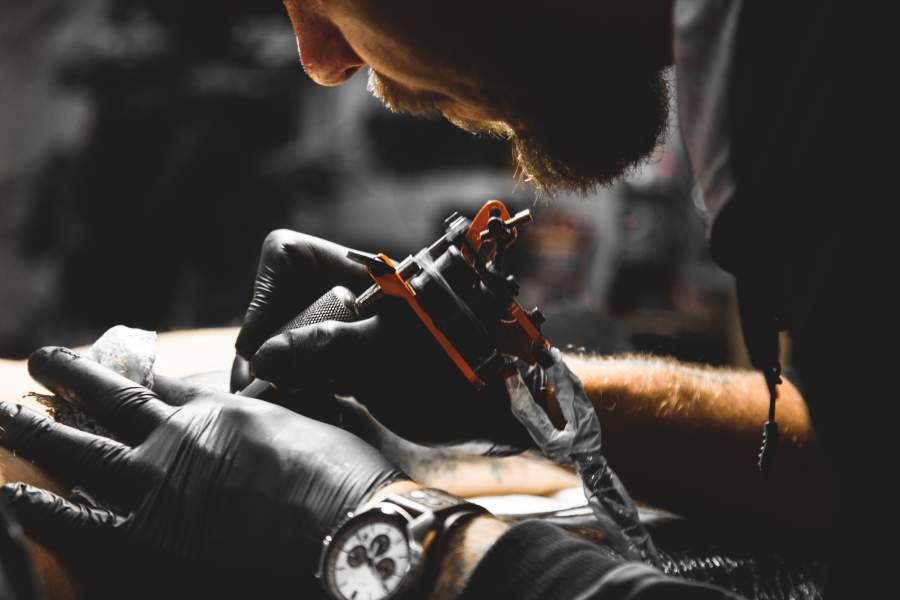Tätowierer mit Gummihandschuhen und Tätowier-Maschine beim Stechen eines Tattoos