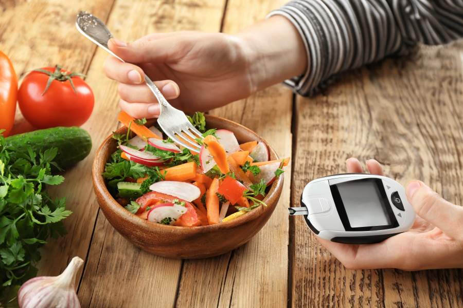 Portion Salat, die mit einer Gabel gegessen wird, in der anderen Hand ein Blutzuckermessgerät