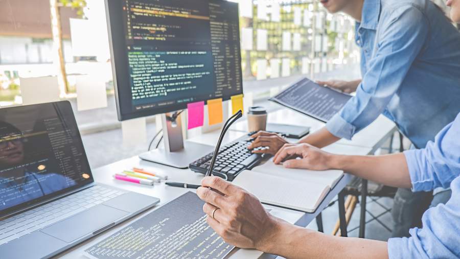 Mehrere Programmierer arbeiten in einem modernen Büro an einem Schreibtisch, auf dem mehrere Bildschirme stehen.