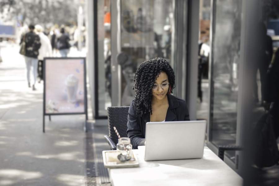 Junge Frau arbeitet an einem Laptop im Außenbereich eines Straßencafés