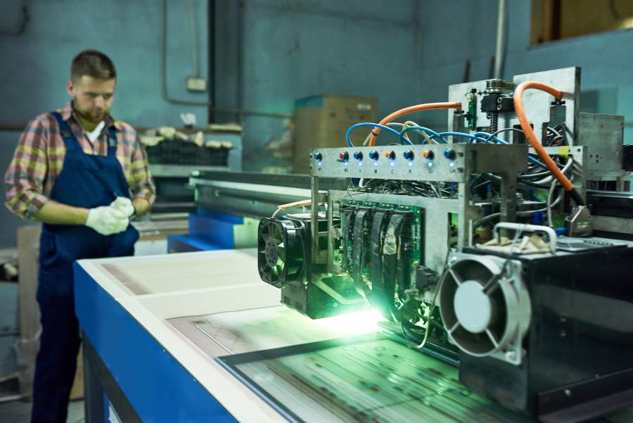 Arbeiter überwacht eine Lasermaschine bei Gravierarbeiten in einer Werkhalle