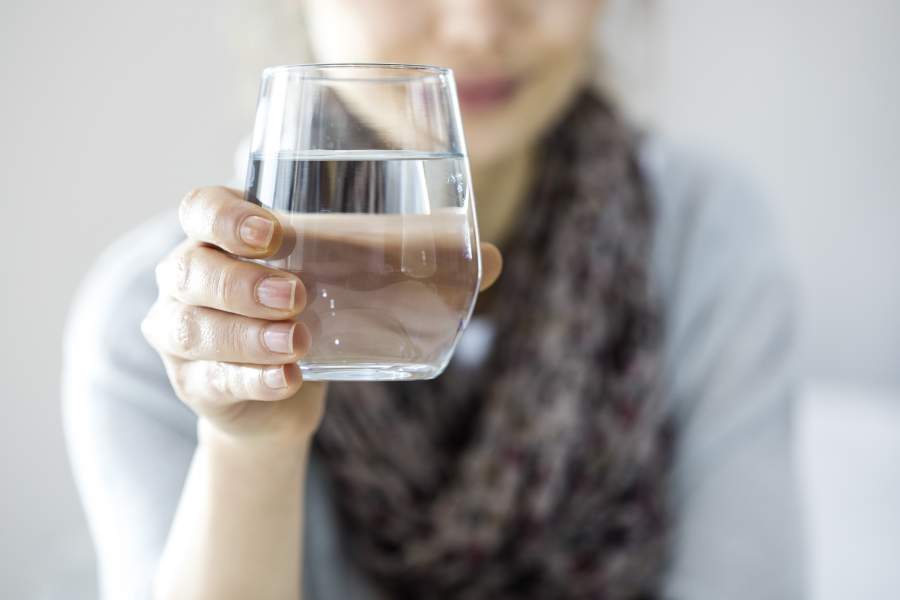 Frau hält ein Glas Wasser in den Bildmittelpunkt