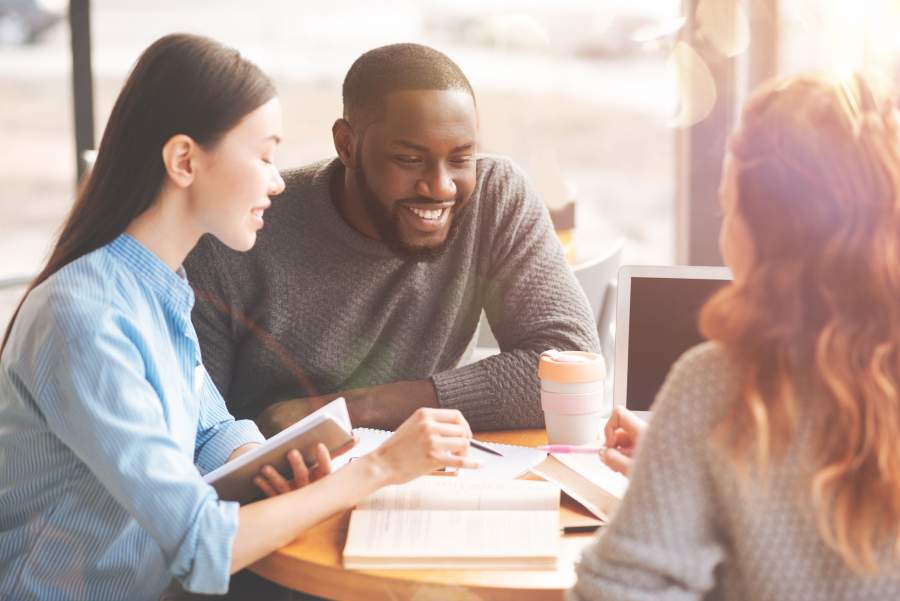 Internationale Studierende in einem fröhlichen Gespräch, auf dem Tisch sind Lernunterlagen und ein Kaffeebecher