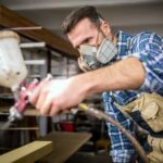 Handwerker bearbeitet Holz mit Sprühfarbe und trägt eine Atemschutzmaske zum Schutz vor Gesundheitsrisiken für die Atemwege
