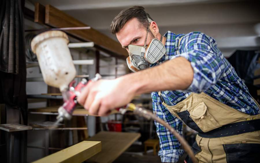 Handwerker bearbeitet Holz mit Sprühfarbe und trägt eine Atemschutzmaske zum Schutz vor Gesundheitsrisiken für die Atemwege