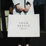 Papiertasche mit dem Aufdruck „Your Design here“ gehalten von den Händen einer Frau in Mantel