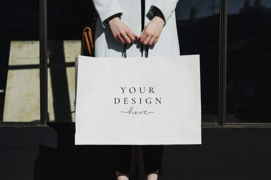 Papiertasche mit dem Aufdruck „Your Design here“ gehalten von den Händen einer Frau in Mantel