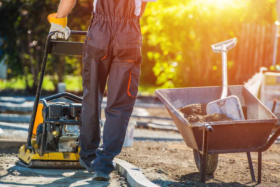 Mann in Arbeitskleidung und Handschuhen zementiert Fundament für Gartenweg