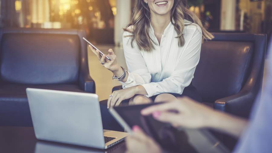 Zwei Business-Frauen sitzen in Leder-Polstermöbeln im Innenbereich und arbeiten mit Tablet, Smartphone und Laptop