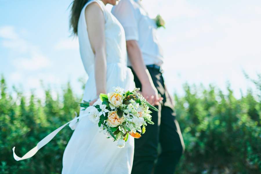 Brautpaar in Brautkleid mit Blumenstrauß und Anzug ohne Sakko in der Natur