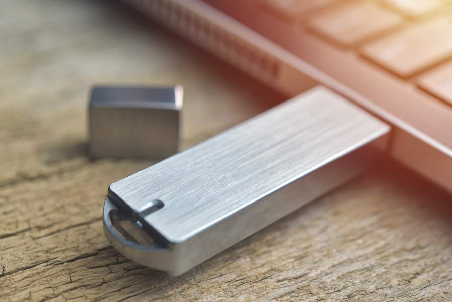 USB-Stick mit Metallhülle steckt in USB-Port eines Laptops auf einem Tisch mit Holzmaserung