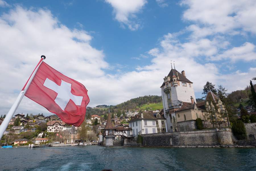 Blick vom Luzerner See auf Ufer und Gebäude, im Bildvordergrund weht die Schweizer Flagge im Wind