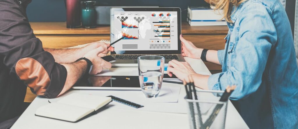 Mann und Frau sitzen vor Bildschirm und betrachten Grafiken zum Monitoring von Online Marketing