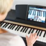 Frau beim Online Klavierunterricht mit Tablet am Klavier