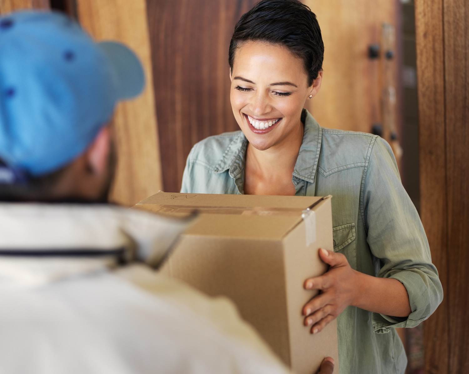 Lächelnde Frau bekommt Paket in Karton Verpackung an der Tür überreicht