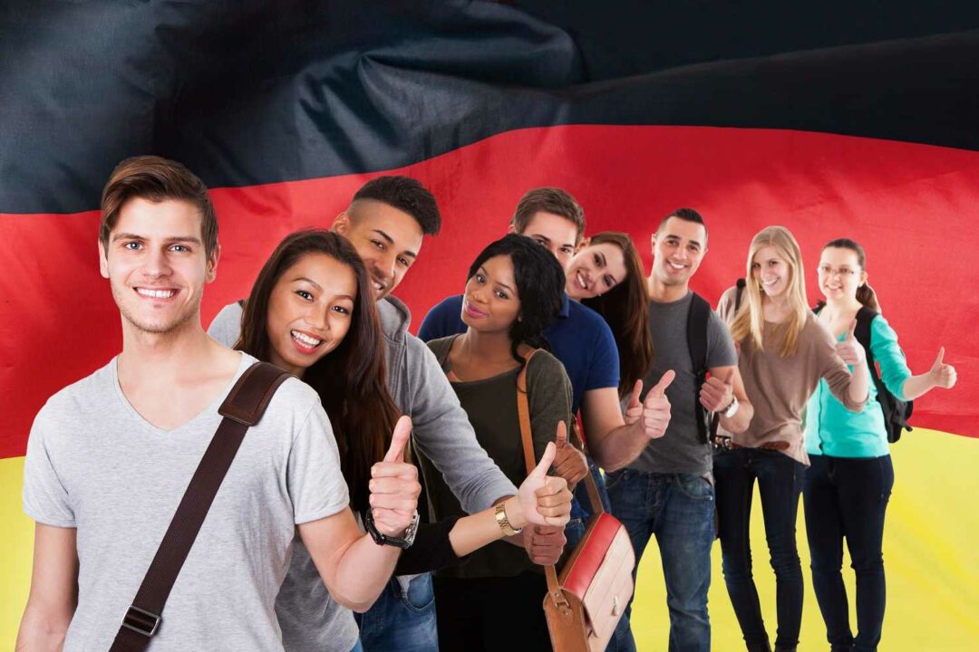 Junge Menschen verschiedener Herkunft stehen fröhlich vor Deutschlandflagge und wollen Deutsch lernen