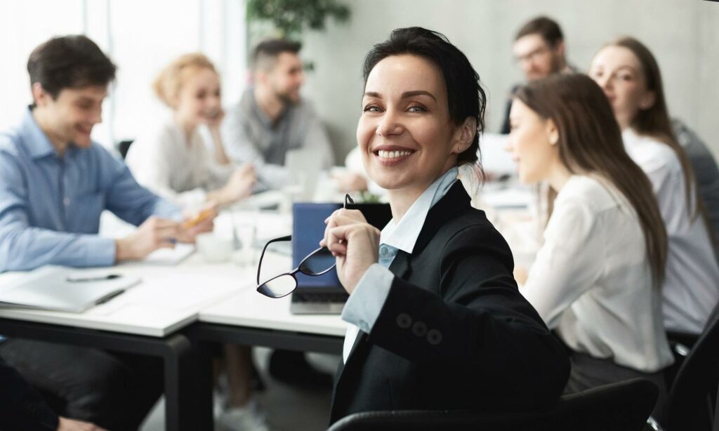 Managerin lächelt bei einem Meeting in die Kamera und zeigt wie gesund leben geht
