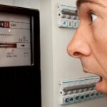 Mann schaut erschrocken auf Stromzähler und muss Stromkosten im Haushalt reduzieren