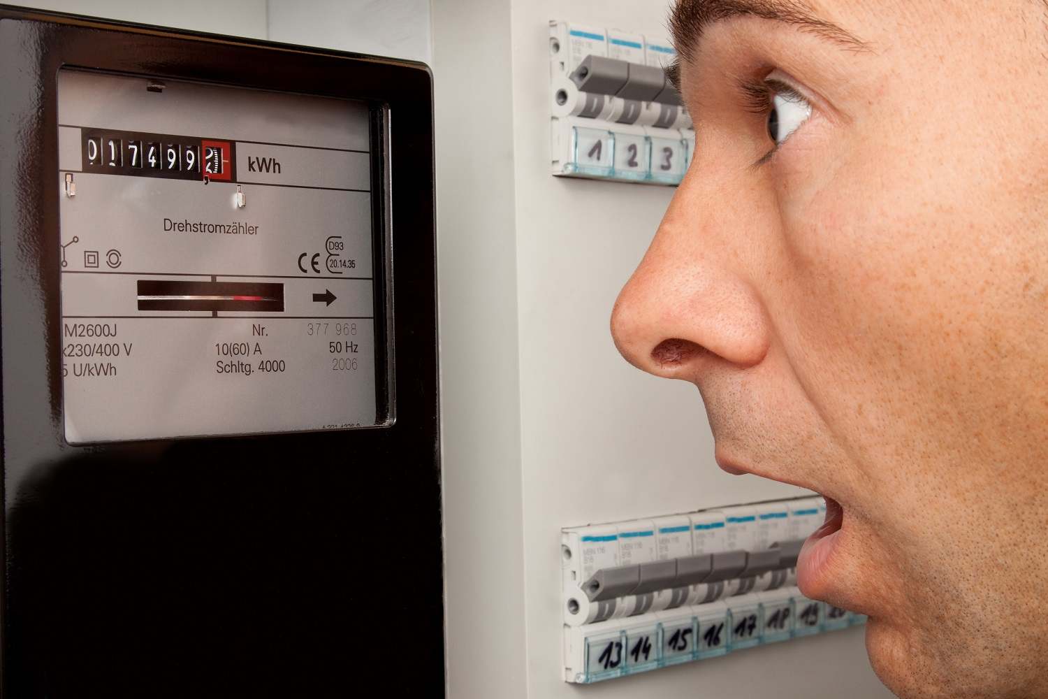 Mann schaut erschrocken auf Stromzähler und muss Stromkosten im Haushalt reduzieren
