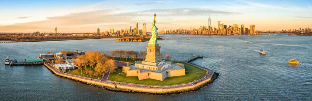 Luftpanorama der Freiheitsstatue vor der Skyline von Jersey City und New York City bei Sonnenuntergang